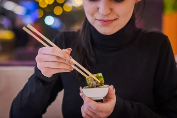 Sierkussen Nagelstudio Eating sushi in the restaurant, a woman with a perfect manicure using chopsticks takes a piece of roll, enjoying tasty and healthy food, traditional Asian dish close up  © Albert