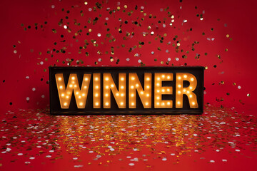A sign that says "winner" is lit up in a red background with confetti. The sign is surrounded by confetti, which adds to the celebratory atmosphere. Concept of achievement and success