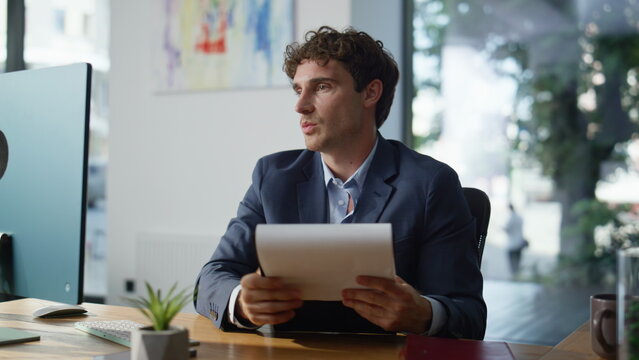Businessman holding papers talking to webcam laptop online in open space closeup