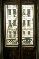 Wooden vintage bed in a bedroom with patterned wallpaper. Worn out boots and an old-fashioned carpet on a wooden floor. Ancient sleeping room and home interior.