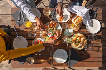 Friends enjoying their vacation, eating lunch outdoor terrace of a glamping resort surrounded by beautiful nature. Top down view