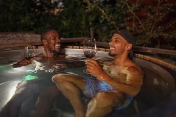 Luxury experience in nature, a gay male couple enjoying the private outdoor hot tub at night. Vacation, resort, hotel and romance concepts.