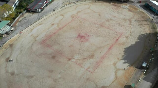 Slow pan out to reveal ground and surrounding community and mountain range - aerial drone shot Queenstown Oval, Tasmania, Australia - famous gravel oval
