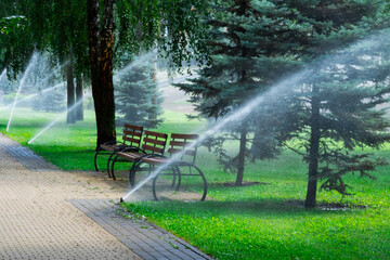 Sprinkler of automatic watering over green grass in the parks.