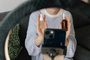 Middle-aged woman beauty blogger filming skincare product unboxing at home with ring light....