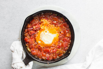 Overhead view of poached egg in tomato sauce, top view of fried egg and tomatoes in a cast iron skillet