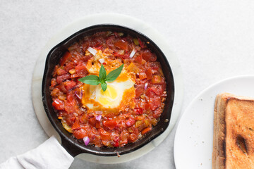 Overhead view of poached egg in tomato sauce, top view of fried egg and tomatoes in a cast iron...