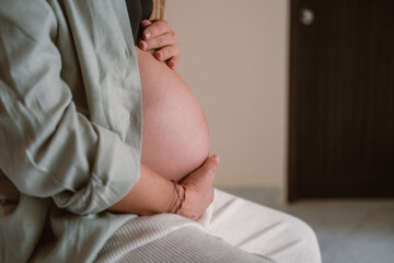 Side shot of pregnant woman belly She is sitting on bed in her bedroom and gently stroking her...