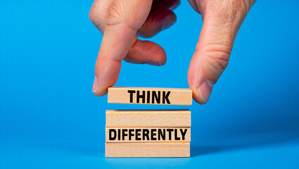 A hand places a wooden block with the word think on top of a stack of blocks that read differently