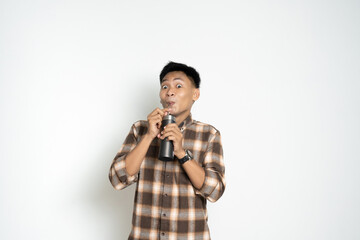 cheerful Asian man drinks from a bottle with a fun expression, wearing a casual plaid shirt, in front of a plain white background.