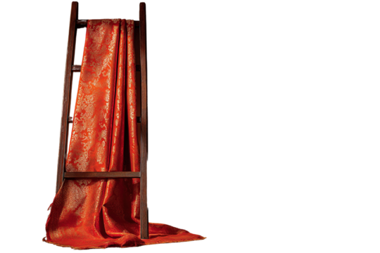 Elegant orange brocade fabric draped artistically on a wooden ladder against black backdrop