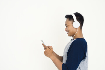 A young man smiles while using his smartphone and wearing white headphones, highlighting modern digital leisure, listening to music, and online connectivity.