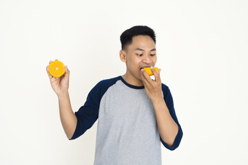 Man Enjoying Fresh Orange in Casual Outfit Against White Background