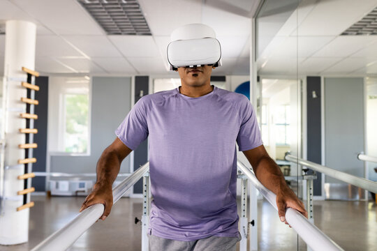 Therapy patient grasping parallel bars while wearing VR headset in therapy room, mirrored wall
