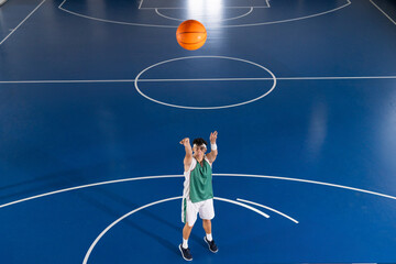 Male athlete wearing green jersey shooting orange basketball from freethrow line on blue court