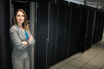 Professional woman standing with crossed arms in data center corridor near server racks, copy space