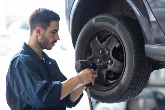 Male mechanic working on lug nuts using impact wrench by hydraulic lift in garage, copy space