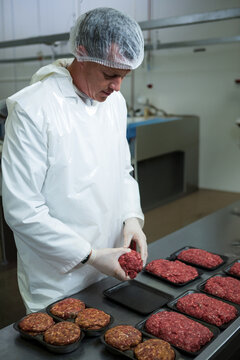 Mid adult man wearing hairnet and gloves forming meat patties on table in food processing facility