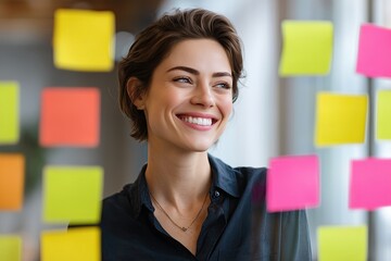 Smiling woman planning and brainstorming in office using sticky notes on glass wall