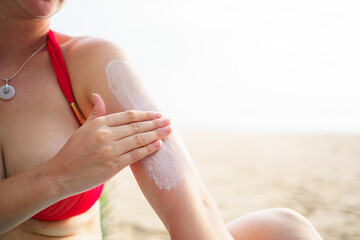 Caucasian woman applying sunscreen at the beach, preparing for sunbathing and water activities.