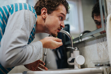 A young individual engages in morning hygiene by washing his face at a basin, emphasizing self-care routines and personal health in a domestic setting.