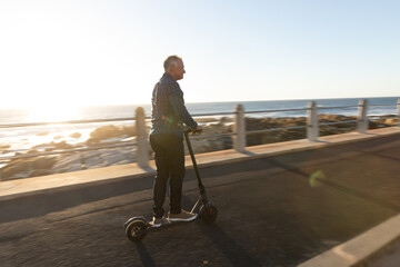 Electric scooter gliding along coastal path under low sun creating lens flare and long shadows