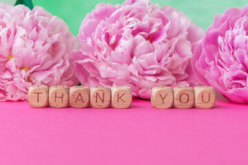 Pink peonies and message thank you on wooden blocks on vibrant pink surface