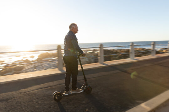 Electric scooter gliding along coastal path under low sun creating lens flare and long shadows