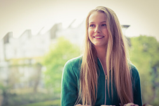 Teenage girl standing on balcony wearing green hoodie smiling looking right by railing, copy space
