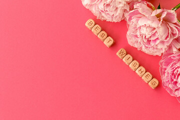 Pink floral greeting card with best wishes wooden blocks and peony flowers. Copy space