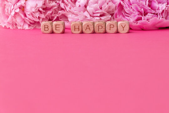 Be happy message with wooden blocks on pink background with pink flowers. Copy space