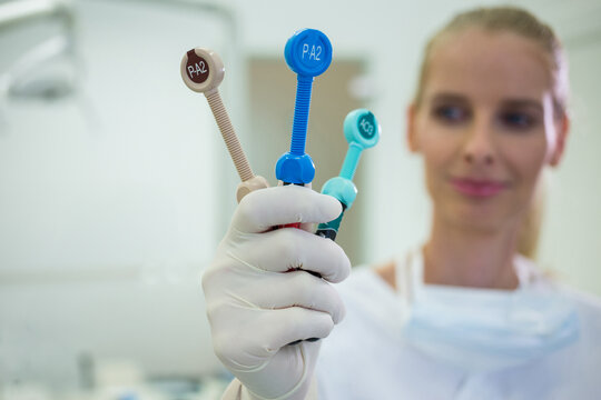 Mid adult female dentist wearing latex glove holding three endodontic files in treatment room