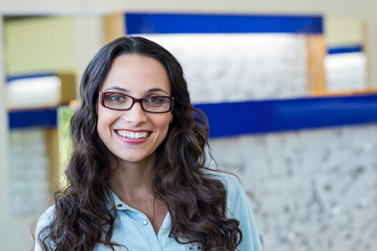 Woman retail associate wearing eyeglasses smiling at camera in optical store with frame displays