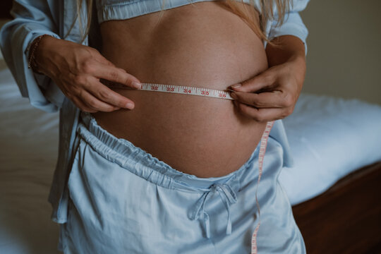 Close-up of a pregnant woman's big belly, measuring her belly with an inch tape. Weight gain during pregnancy, monitoring the health of a pregnant woman. - Powered by Adobe