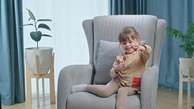 Cute laughing toddler girl liking lolipop and showing like and dislike sighn, concept of healthy baby feeding without shugar