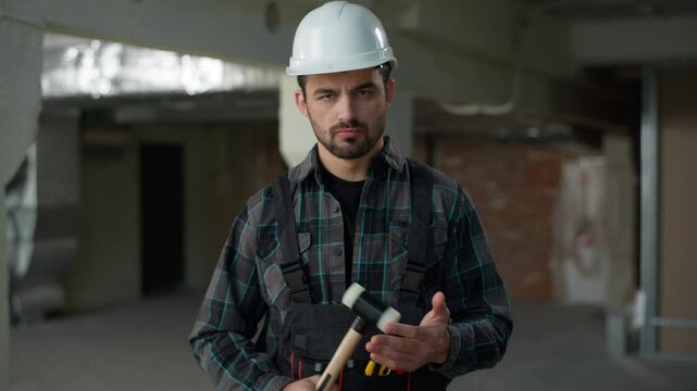 Portrait man builder repairman engineer angry guy hitting hammer on construction site building renovation annoyed industrial architect in uniform foreman handyman male rage looking at camera anger
