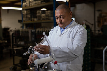 Male technician in white lab coat handling glass distillation apparatus at workstation