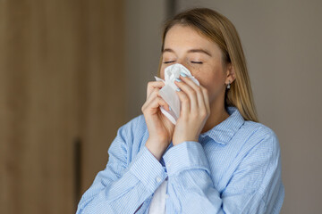 Woman sneezing into a tissue while suffering from a seasonal cold indoors