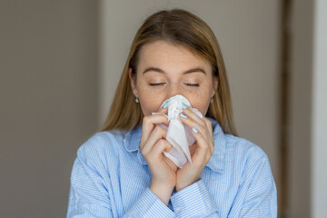Woman blowing nose into tissue while experiencing seasonal allergies or a cold