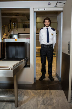 Adult male officer holding wand monitoring metal detector, Xray scanner belt at checkpoint
