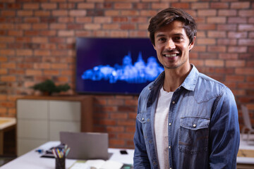 Man standing and smiling in modern office by laptop, monitor and pen holder, copy space