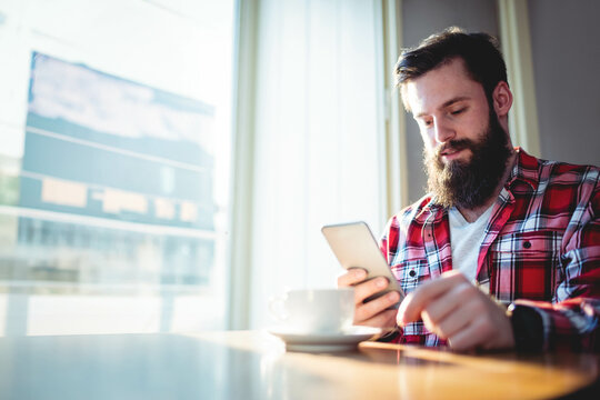 Smartphone resting beside steaming coffee cup on wooden table by bright window in cafe
