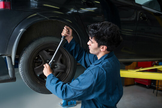 Torque wrench tightening lug nuts on black car wheel on yellow lift arms in repair garage