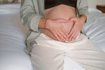 Close up of a pregnant young woman belly as she sits on her bed. She gently strokes her belly and...