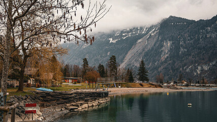 Serene Swiss Lake: Picturesque Shoreline with Alpine Mountains under Cloudy Sky