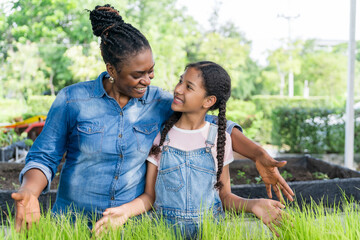 Black mother and daughter care for seedlings in trays on farm. Organic farming, family relationships and environmental education. Parenting, community farming and intergenerational learning.