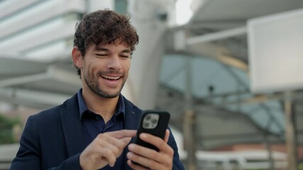 Portrait of Hispanic man corporate employee browses internet on smartphone and smiles on city street. Latin businessman controls commercial data online via cellphone in downtown - Powered by Adobe