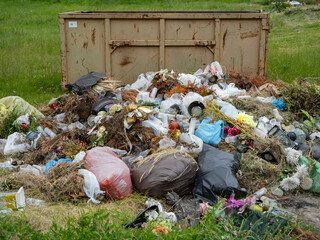 Illegal waste dumping with plastic, flowers, and garden debris overflowing from a container in a...