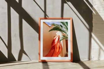 Framed abstract art with red fabric and plant against gray wall in sunlit room