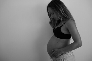 Side view of a pregnant woman with a big belly. She stands in front of a white wall and gently...